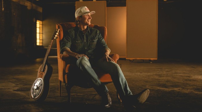 Cooper Alan sat on a chair with a guitar beside him